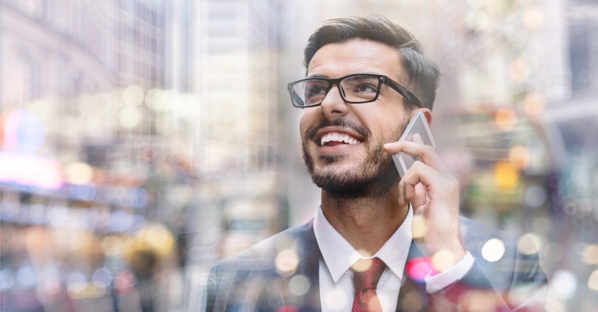 Photo showing a man smiling and using a cell phone on the street, probably talking to a virtual agent using conversational AI and conversational design.