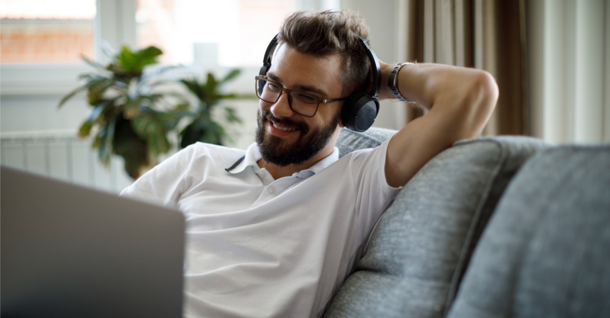 Photo of an internet service subscriber sitting on a couch, wearing headphones, and using a laptop, enjoying his subscriber experience.