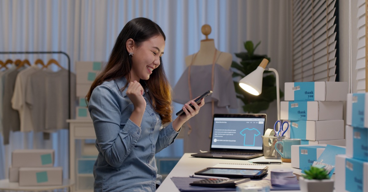 This is a photo of a young woman smiling at her phone while working at her home office, definitely using an IVA to communicate with a virtual contact center.