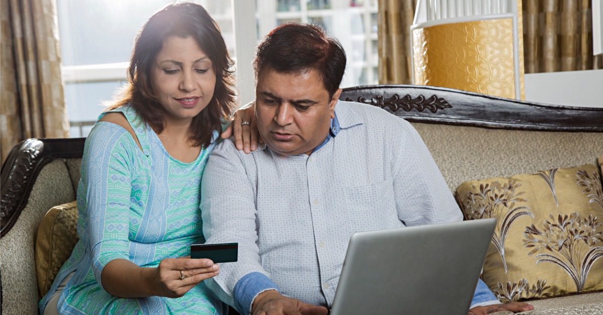 Photo showing a man and woman holding a credit card and using a laptop to engage in personalized banking.
