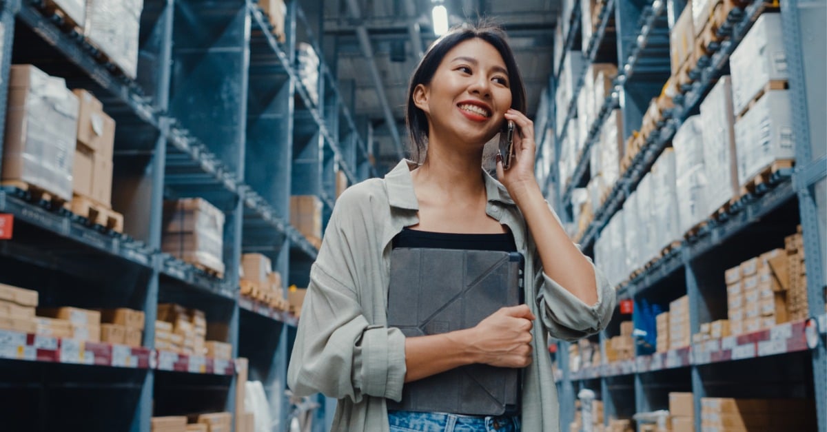 Photo showing a woman in a warehouse smiling and talking to an intelligent virtual agent on her smartphone.