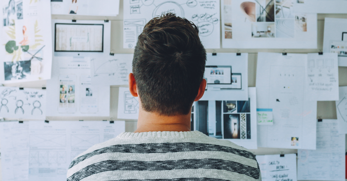 Photo of a man staring at papers on a wall as he plans how to train, test, and deploy a conversational AI solution.