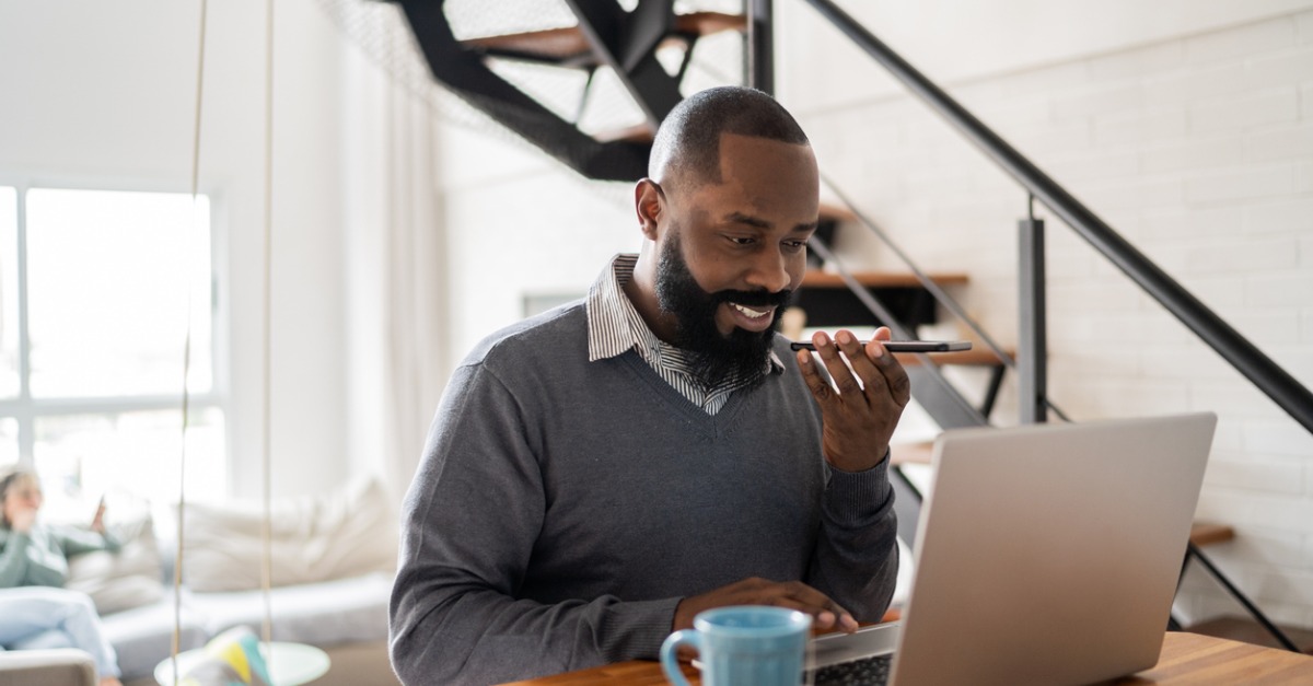 Photo of a man looking at his laptop and talking to an IVA using conversational AI to improve customer experience.