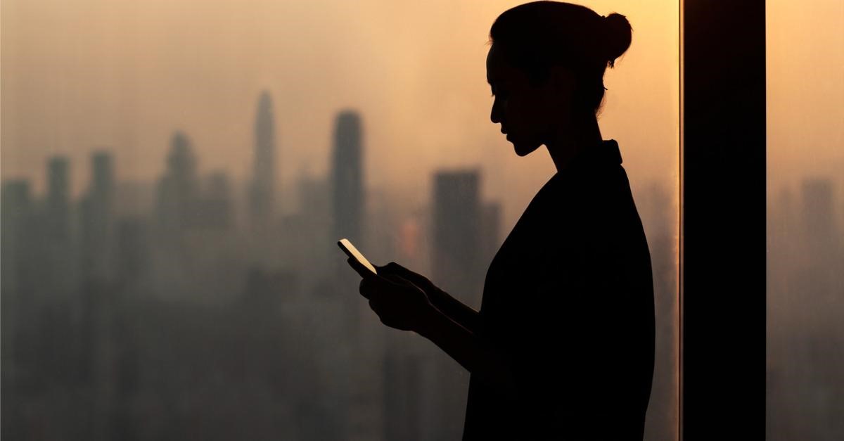 Silhouette of a woman reporting employee misconduct on her smartphone.